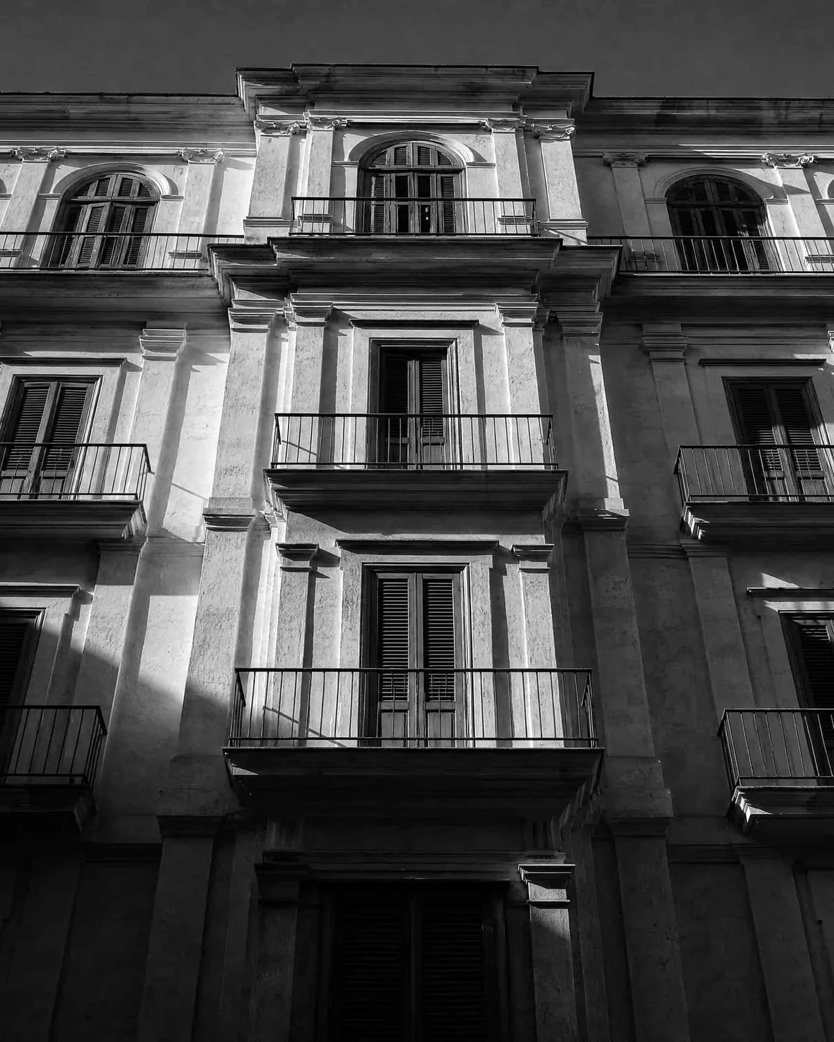 Sonnenbeschienene Altbaufassade mit Balkongeländern und Fensterläden in einer südeuropäischen Stadt, aus der Froschperspektive