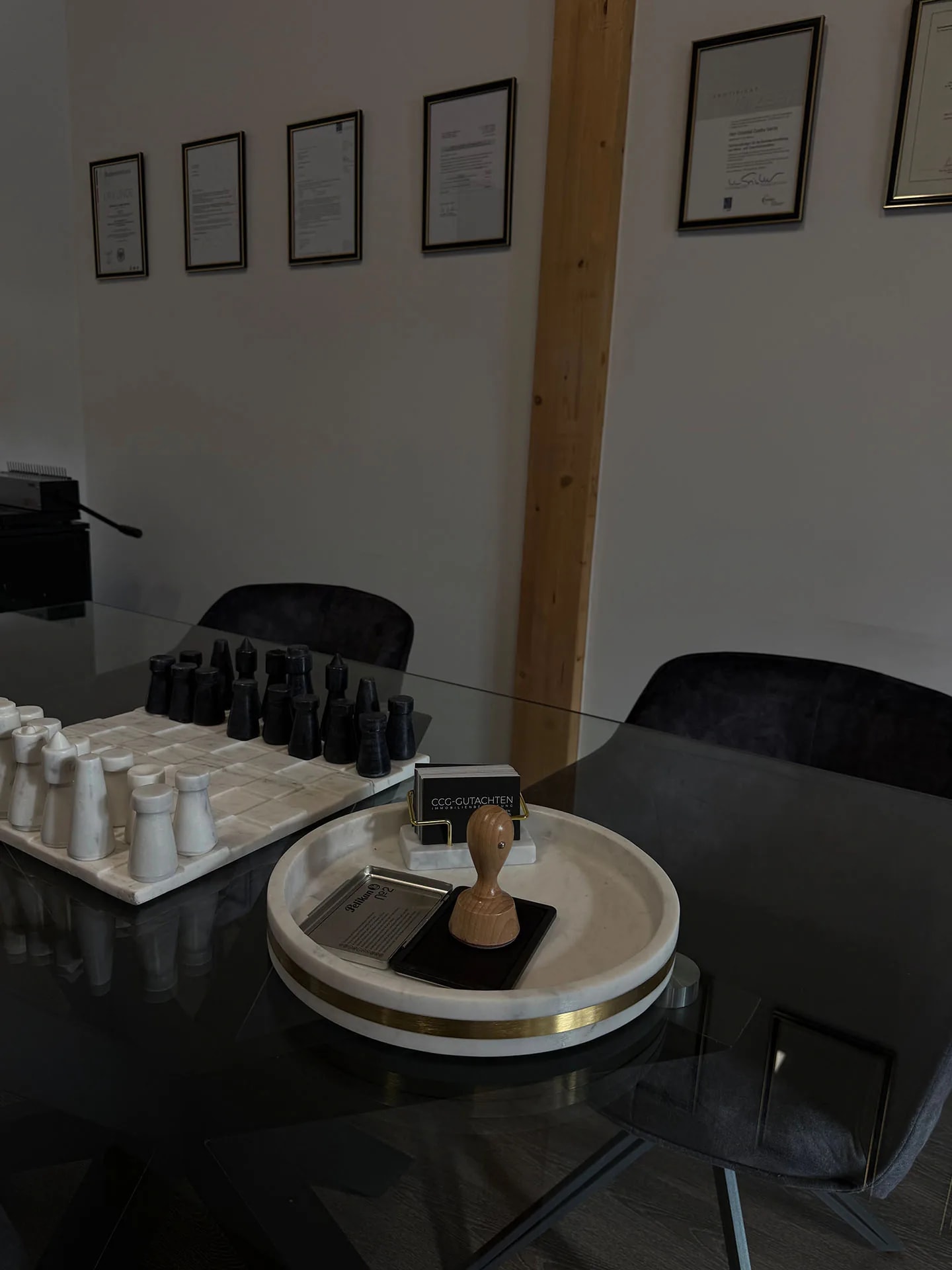 Büro von CCG-Gutachten mit sechs gerahmten Zertifikaten an der Wand, auf dem Besprechungstisch Stempel und Visitenkarten